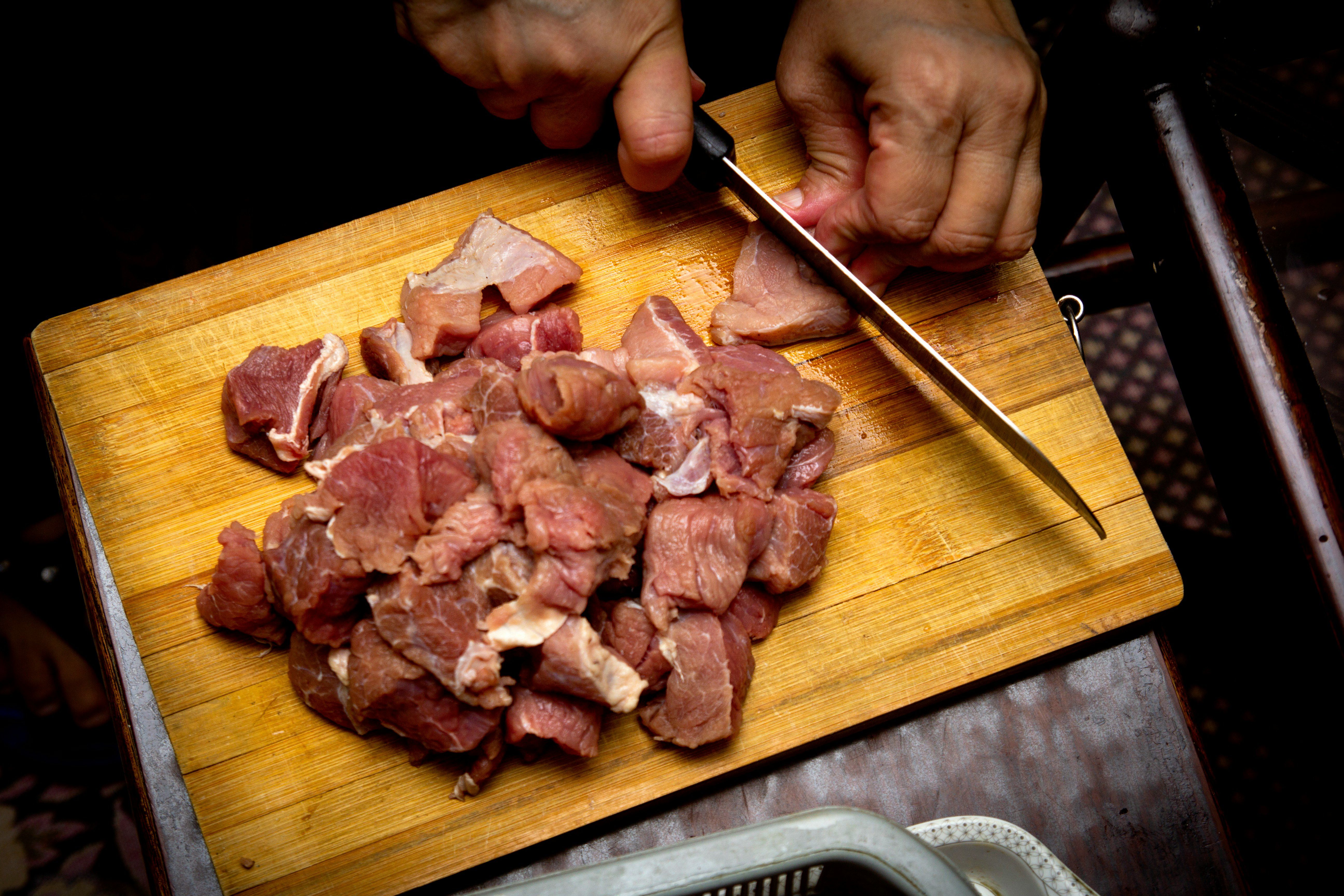 Manos cortando carne en tabla de cocina Manos cortando carne en tabla de cocina